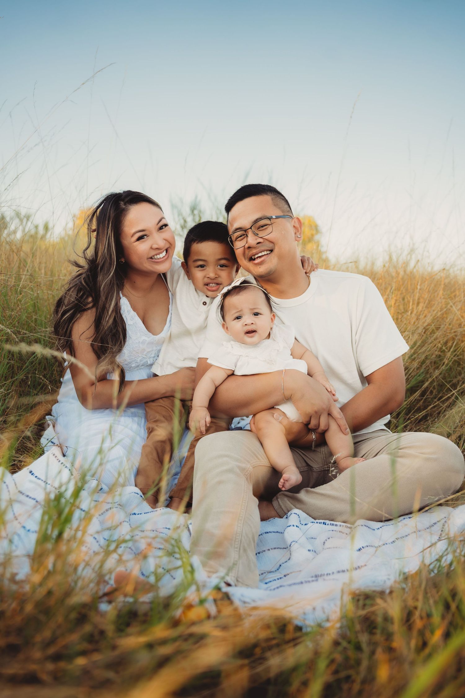 Happy Asian family of four sitting on blanket in golden grass field under clear blue sky. tacoma Washington