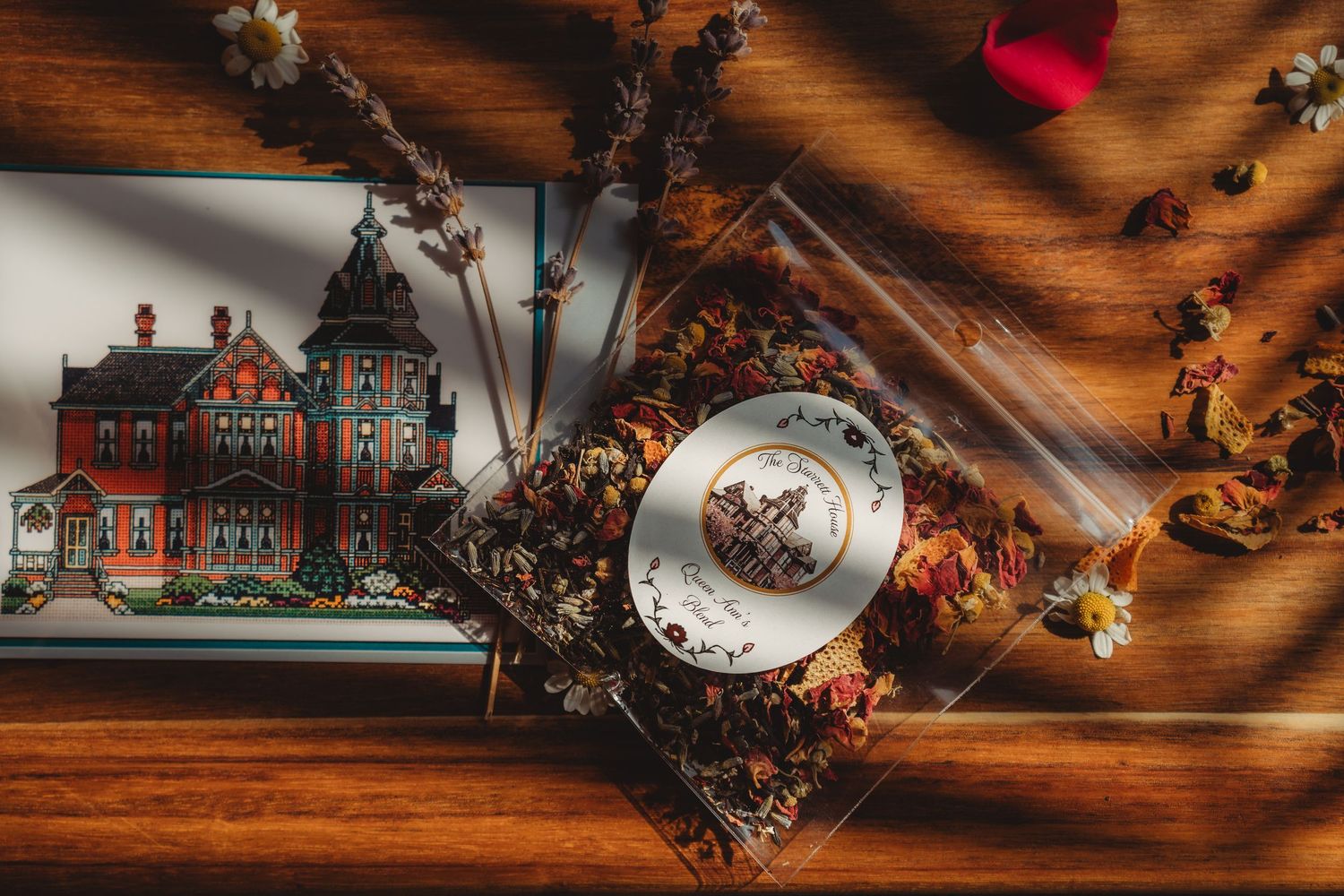 Vintage tea cup with dried flowers and Victorian house illustration on warm wooden background with shadows.