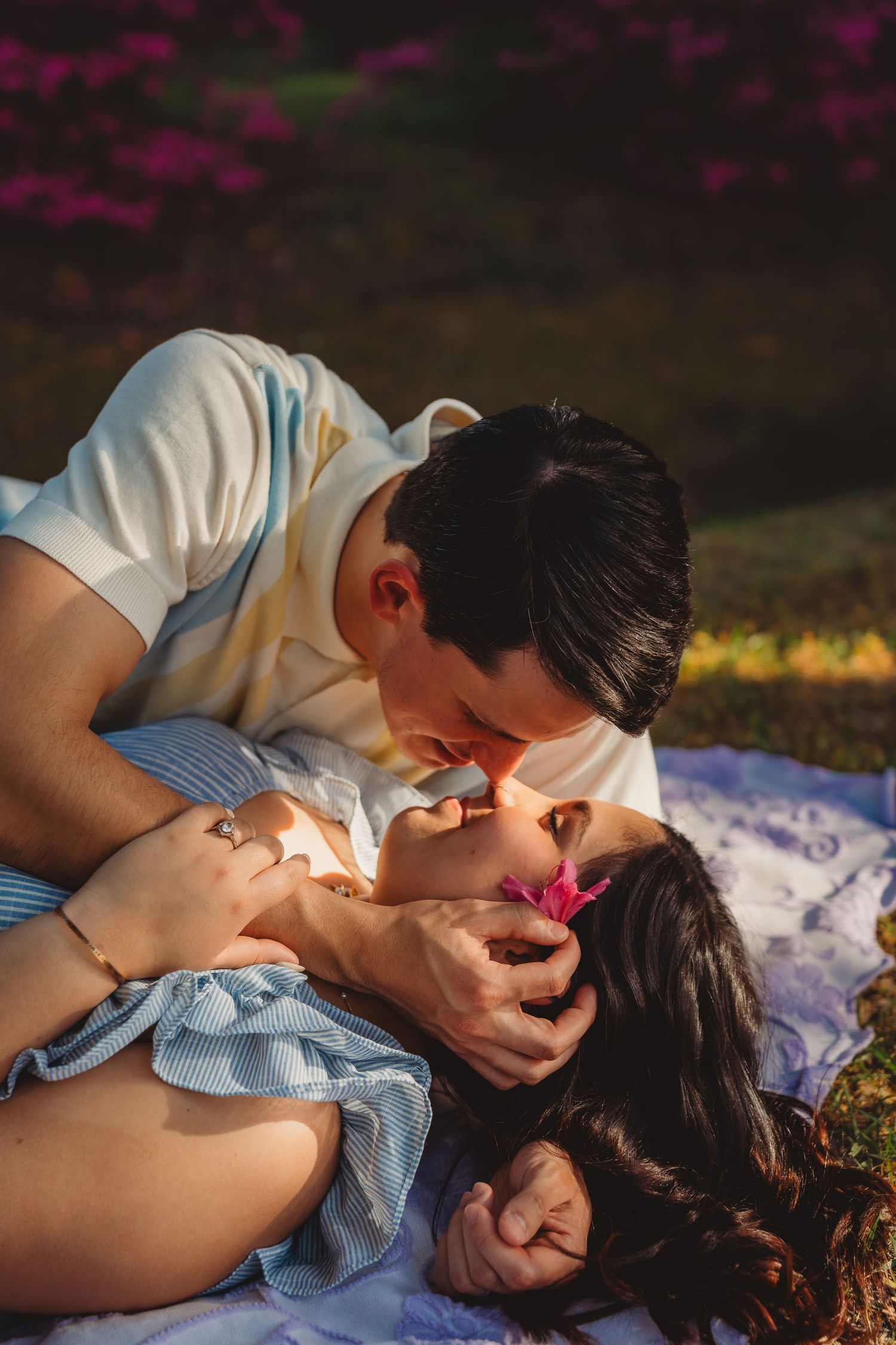 Romantic couple sharing a tender kiss on a blanket in a blooming garden during golden hour.