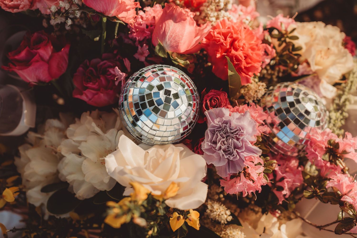 Floral arrangement with pink, white, and red flowers accented by small mirrored disco balls.