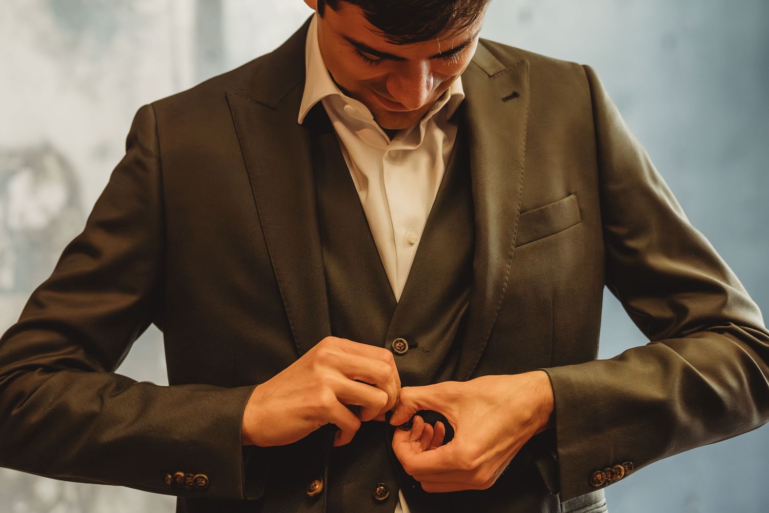 Man in dark suit buttoning his jacket, dressed in formal attire with white dress shirt.