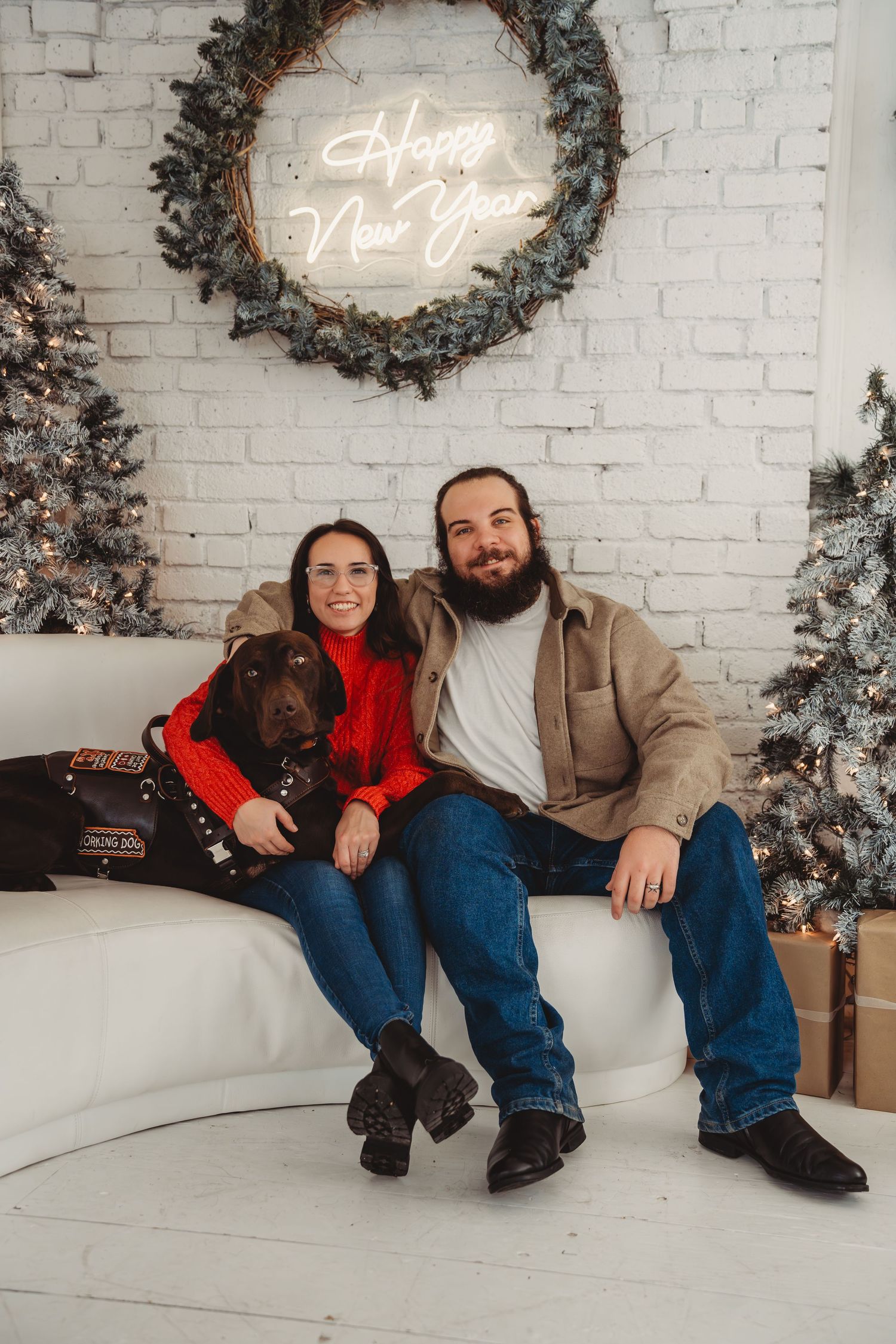 Couple with chocolate Labrador posing on sofa with Happy New Year neon sign. Seattle