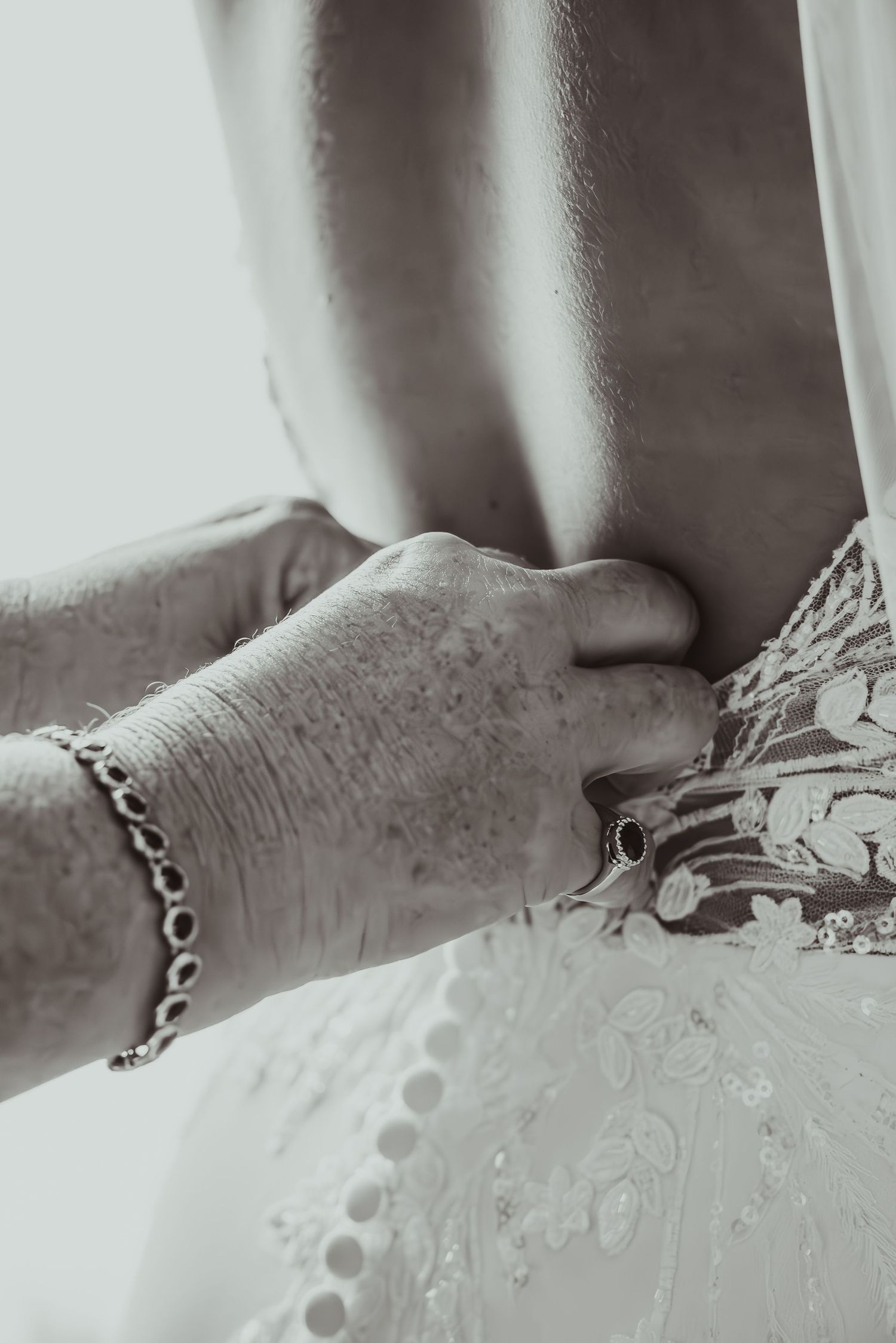 Close-up black and white photo of hands fastening buttons on a lace wedding dress. upland Indiana