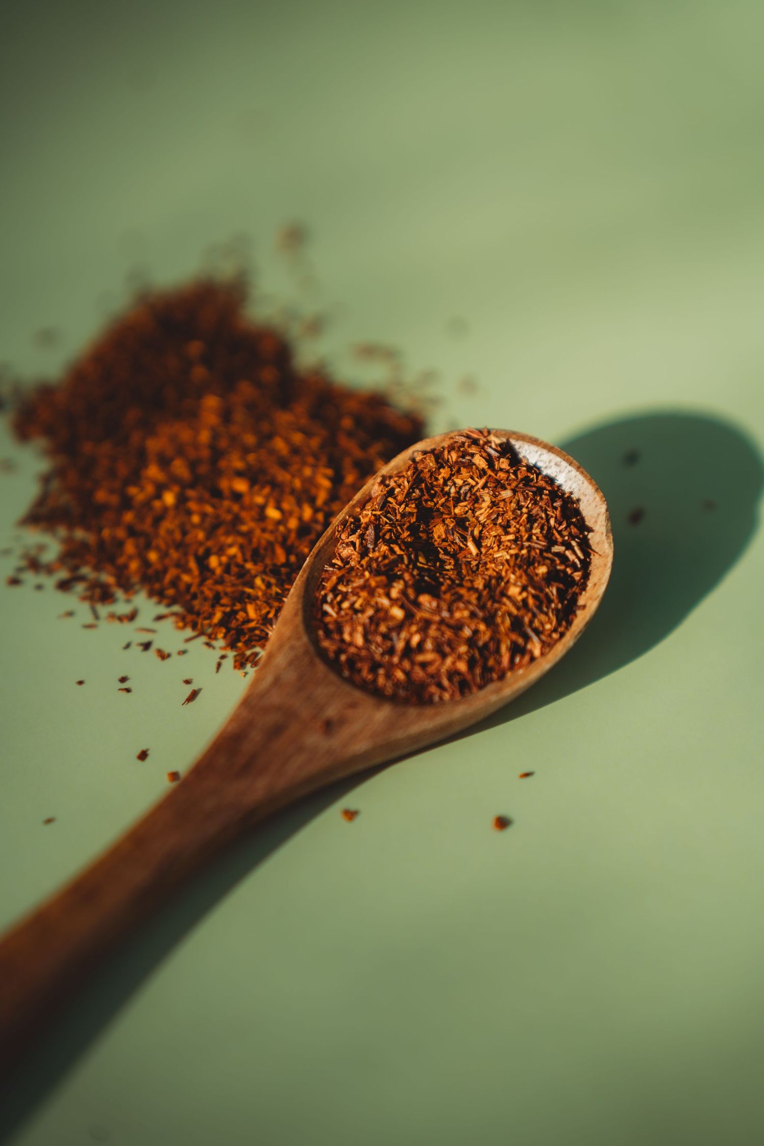 Wooden spoon filled with rooibos tea leaves on a green background with scattered loose tea.Summerville South Carolina