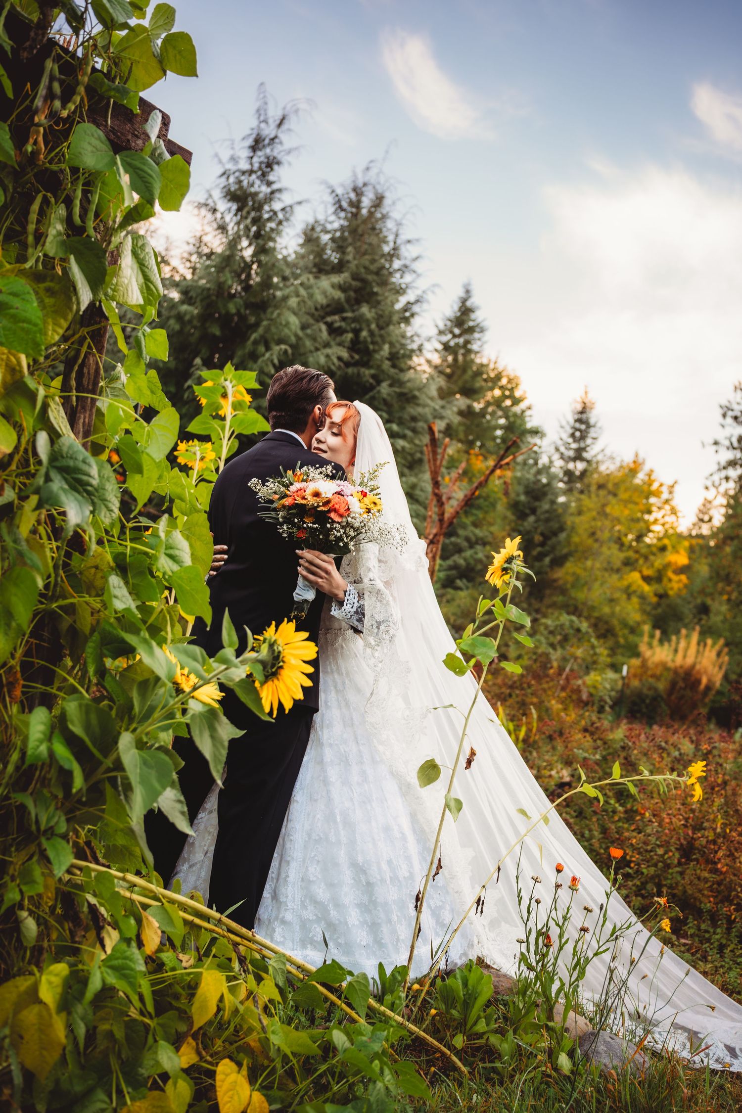 Bride and groom share a romantic kiss surrounded by sunflowers and lush greenery in an outdoor wedding setting. mt hood Oregon