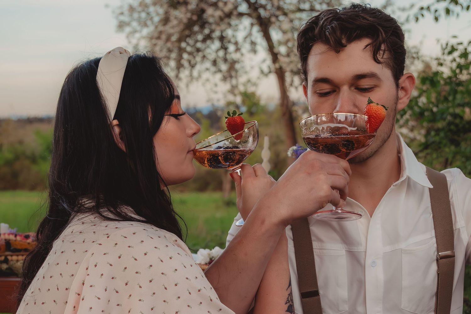 Romantic couple sipping cocktails with strawberries outdoors at sunset during a vineyard date.