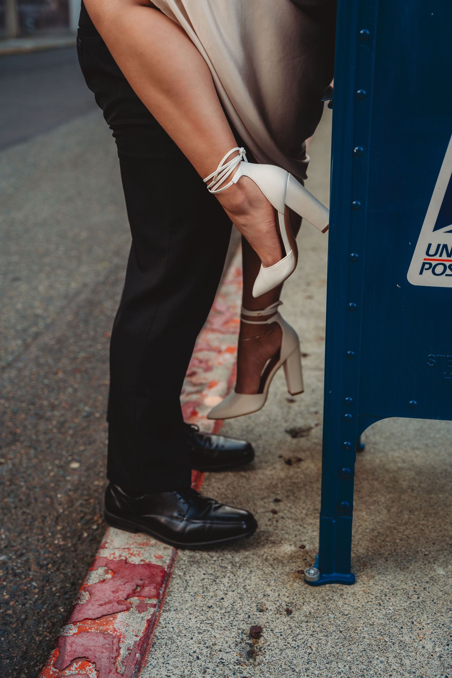 Close-up of a couple embracing near a USPS mailbox, woman holding white heels while wearing brown boots.Charleston South Carolina
