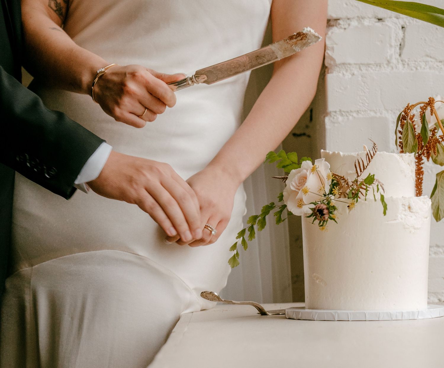 Bride and groom cutting a white wedding cake decorated with pink flowers and greenery together. Seattle