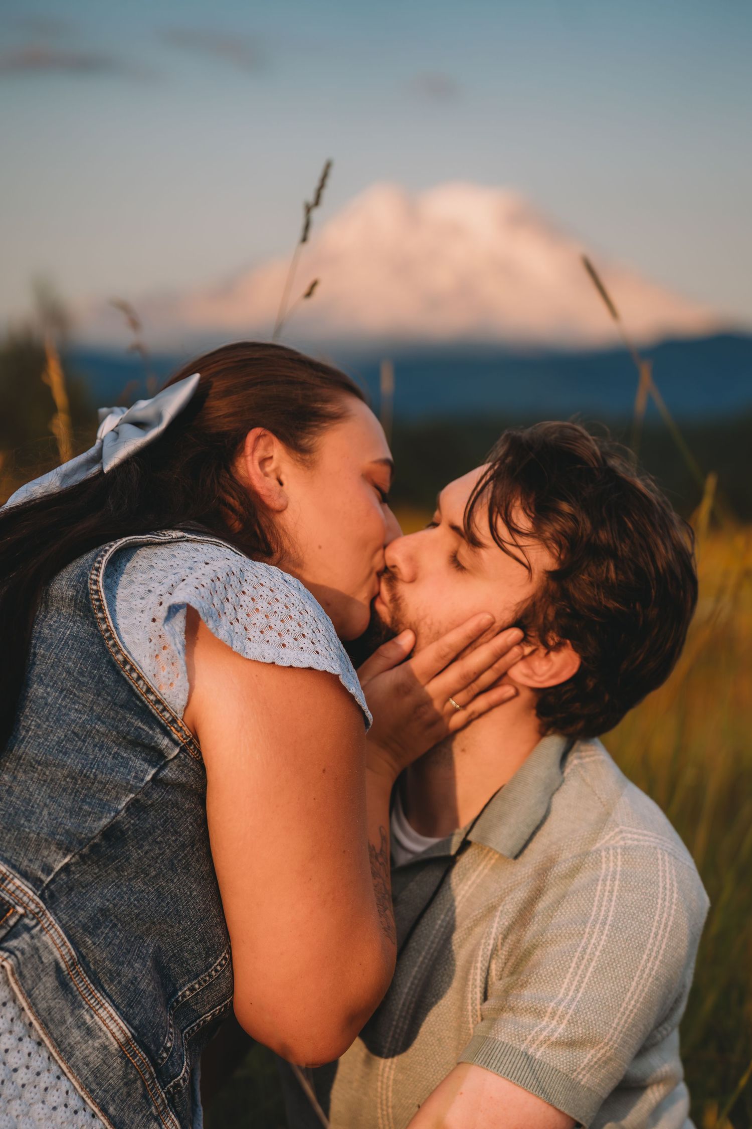 Couple sharing a passionate kiss at golden sunset in a tall grass field with a snow-capped mountain behind. mount Rainer