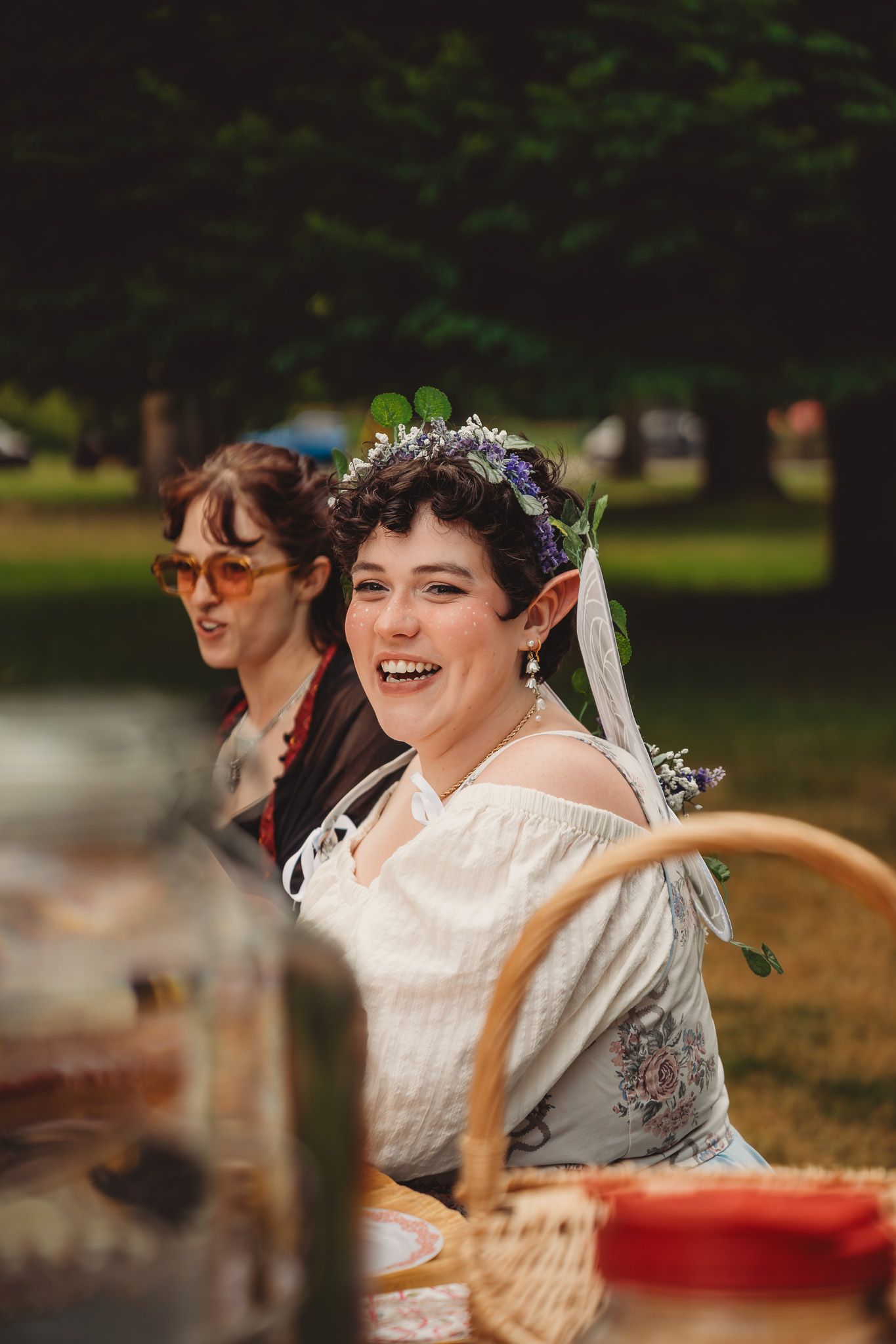 Smiling bride wearing floral crown and veil at outdoor garden wedding celebration with guests in background.