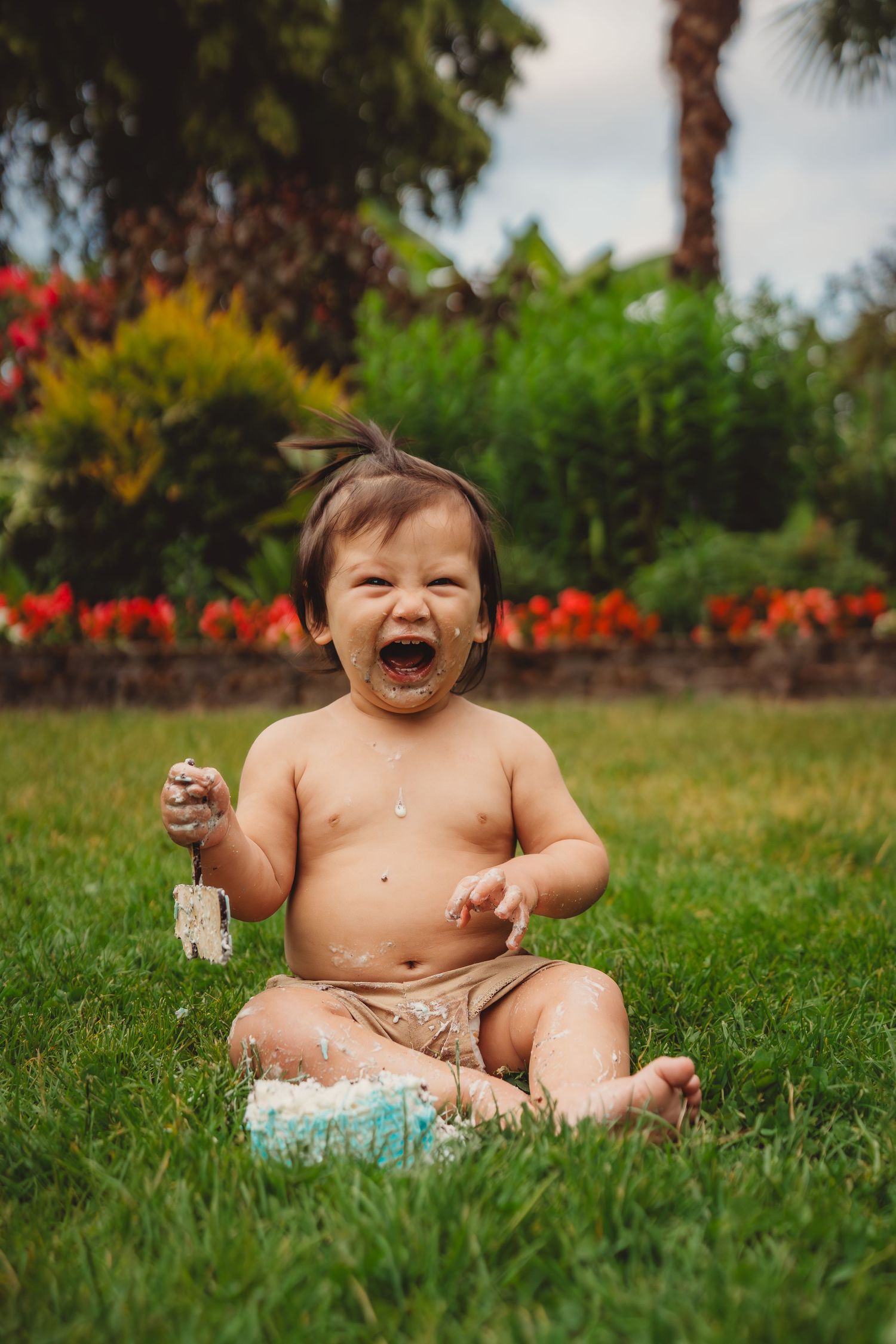 Happy baby sitting on grass laughing with cake smash frosting on face during first birthday celebration. Charleston South Carolina