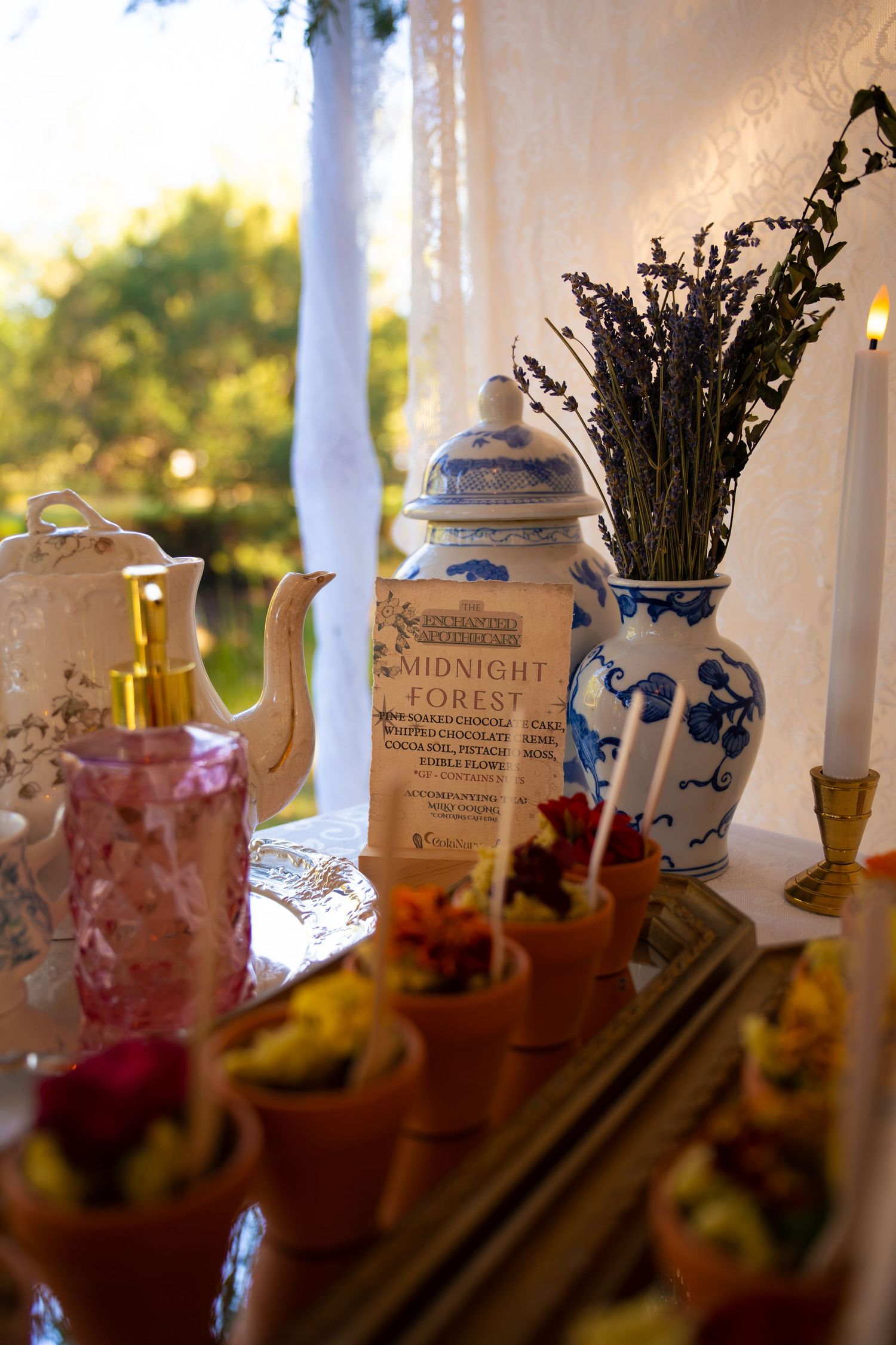 Dessert table with mini terracotta pot treats, a Midnight Forest sign, lavender in a blue-white vase, a lit candle and a vintage teapot.