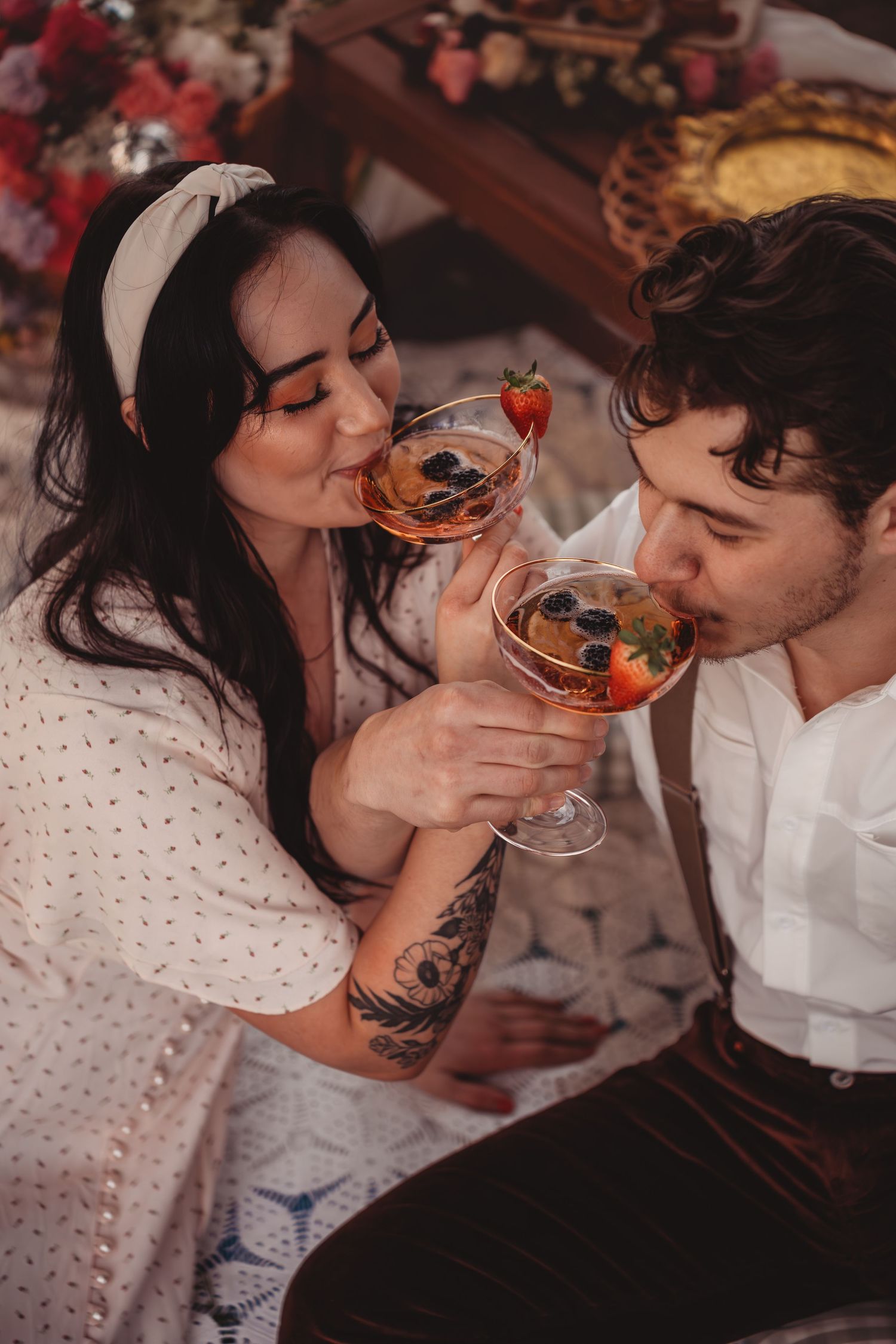 Romantic couple sharing cocktails garnished with fresh berries at an elegant outdoor picnic setting.