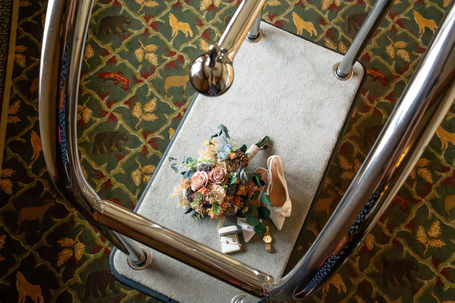 Bridal bouquet with peach roses and greenery displayed on a chair with ballet flats and decor against patterned wallpaper.