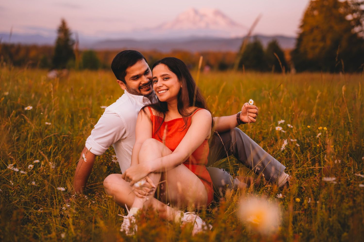 Couple sitting together in a wildflower meadow at sunset with a snow-capped mountain in the background.