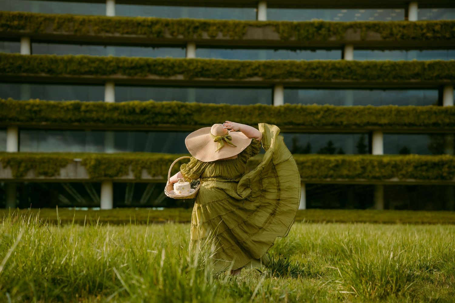 Person in green wrap and pink hat sitting in lush green grass in front of tiered hedge wall. fedrallway Washington