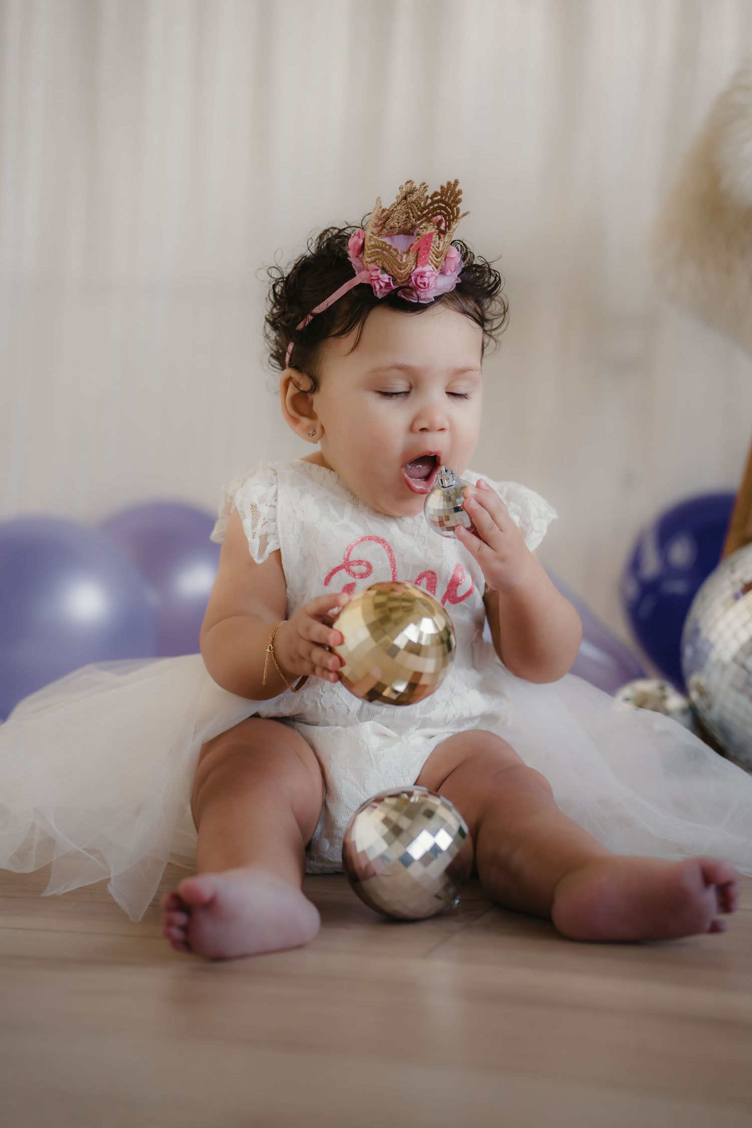 Adorable baby girl in white dress and crown headband playing with disco balls at birthday party.Summerville South Carolina