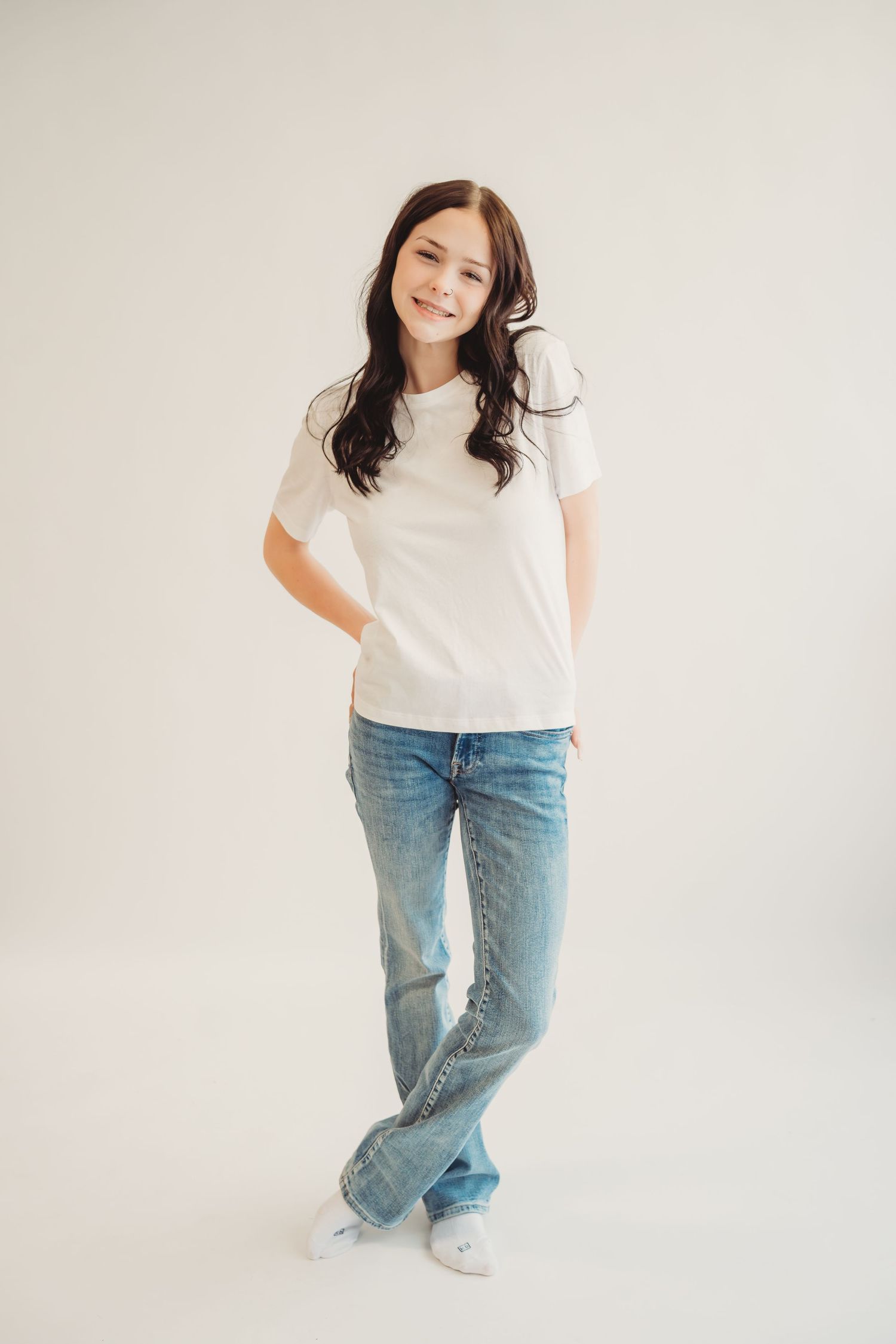 Smiling young girl in white t-shirt and blue jeans posing against a light background.