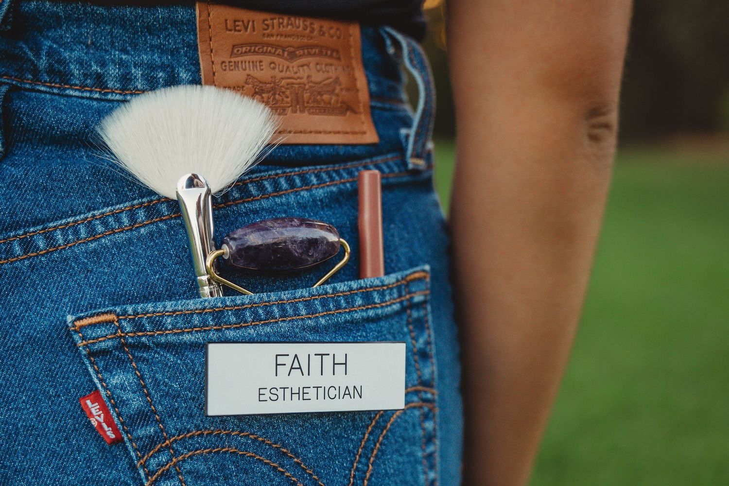 Close-up of Levi jeans back pocket with makeup brushes and an esthetician name tag.