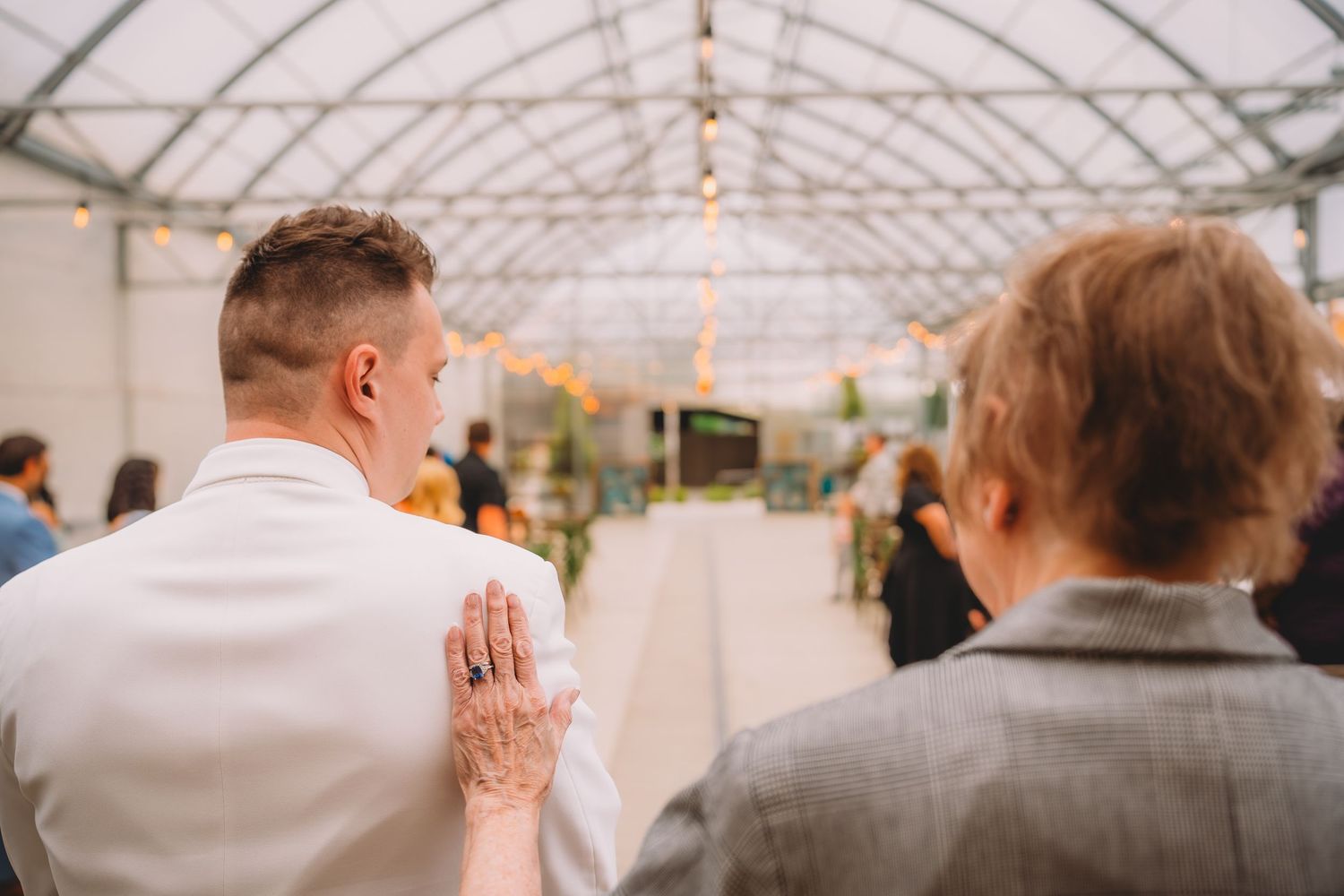 Couple holding hands with henna tattoo at an indoor wedding ceremony in a greenhouse venue.