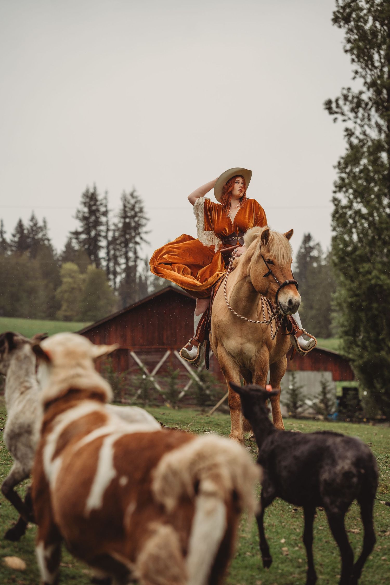 Woman in orange dress riding a horse surrounded by cattle on a farm.