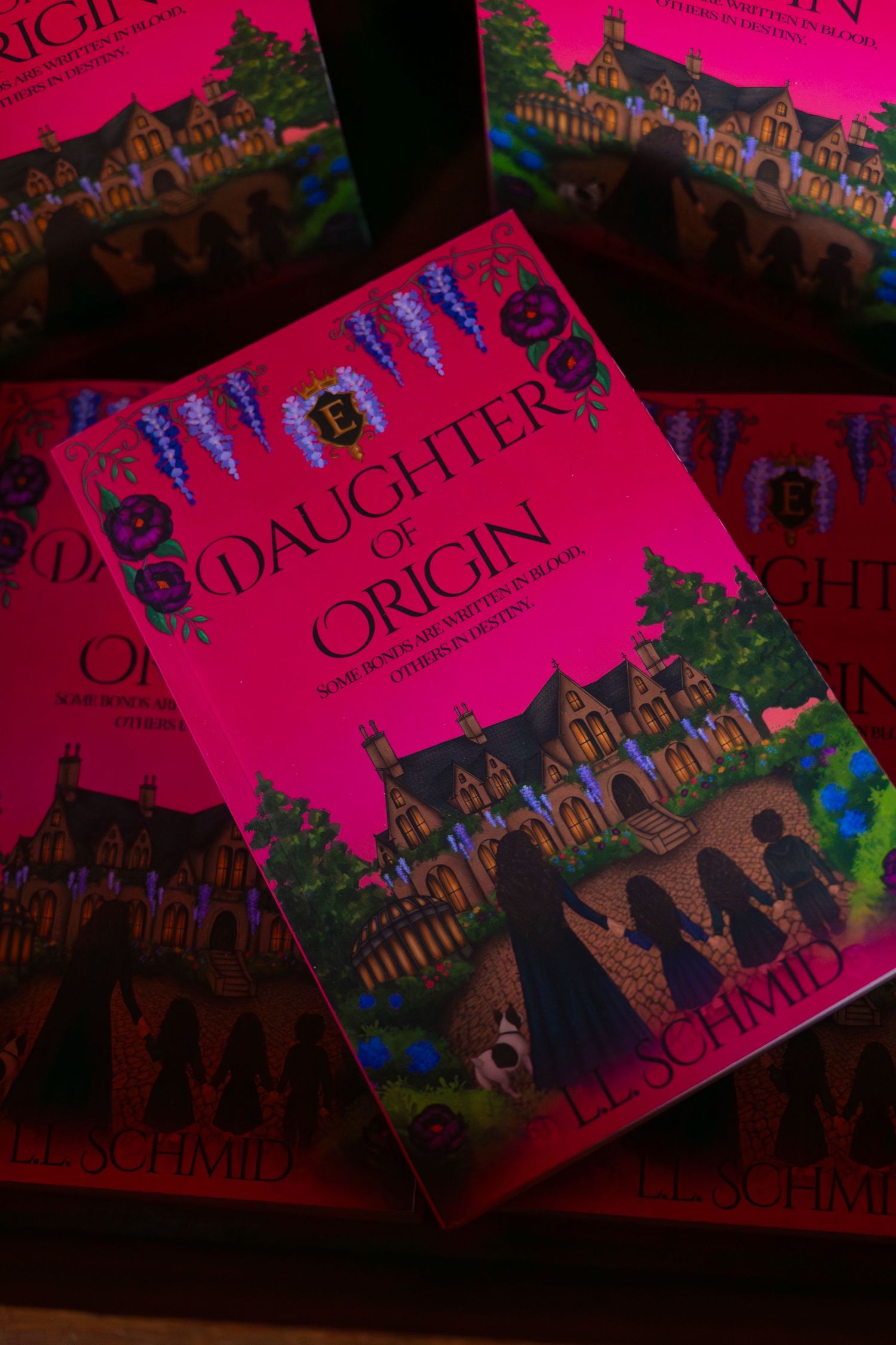 Stack of Daughter of Origin paperback books by L.L. Schmid with pink covers showing a gothic manor, purple flowers, and silhouetted figures.