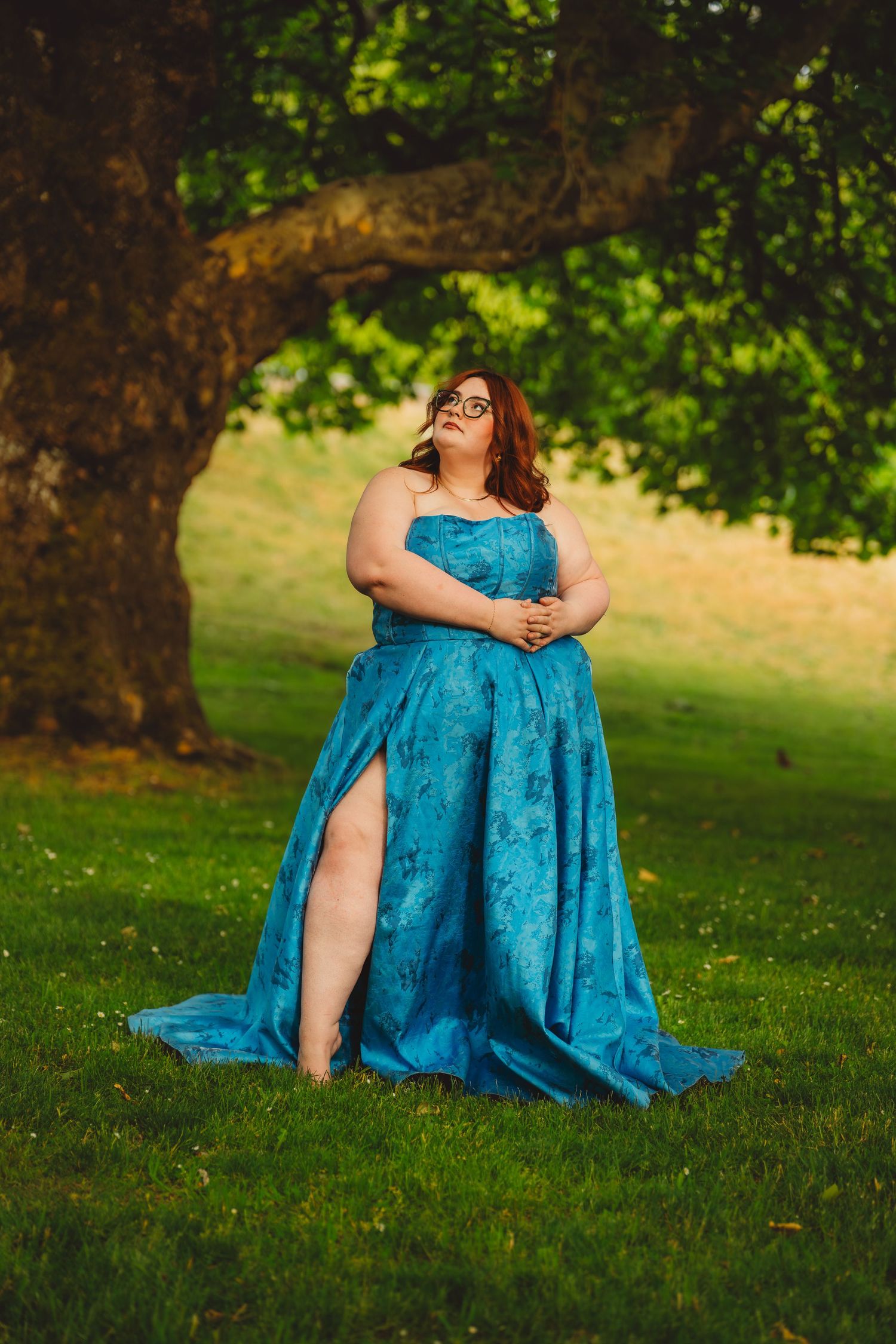 Plus size woman in strapless teal gown with slit stands under tree in green park. Charleston South Carolina