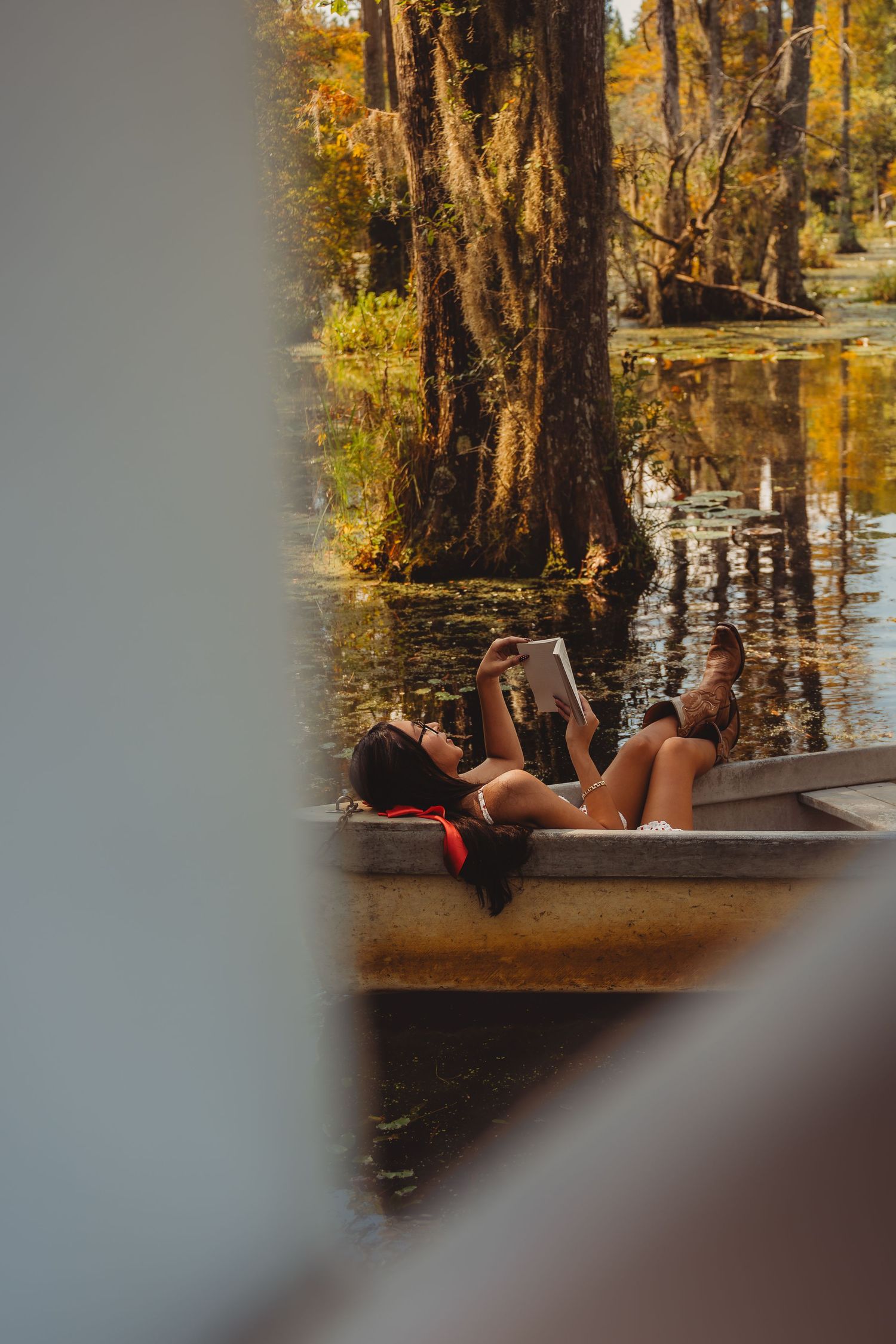 Woman relaxing in a boat reading a book on a serene swamp surrounded by cypress trees.