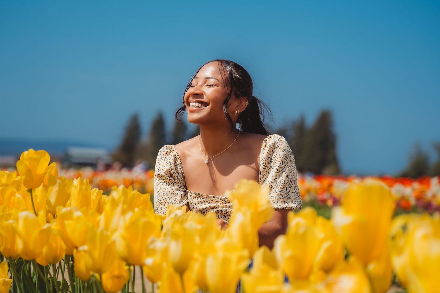 Joyful young woman laughing in vibrant yellow tulip field under clear blue sky.