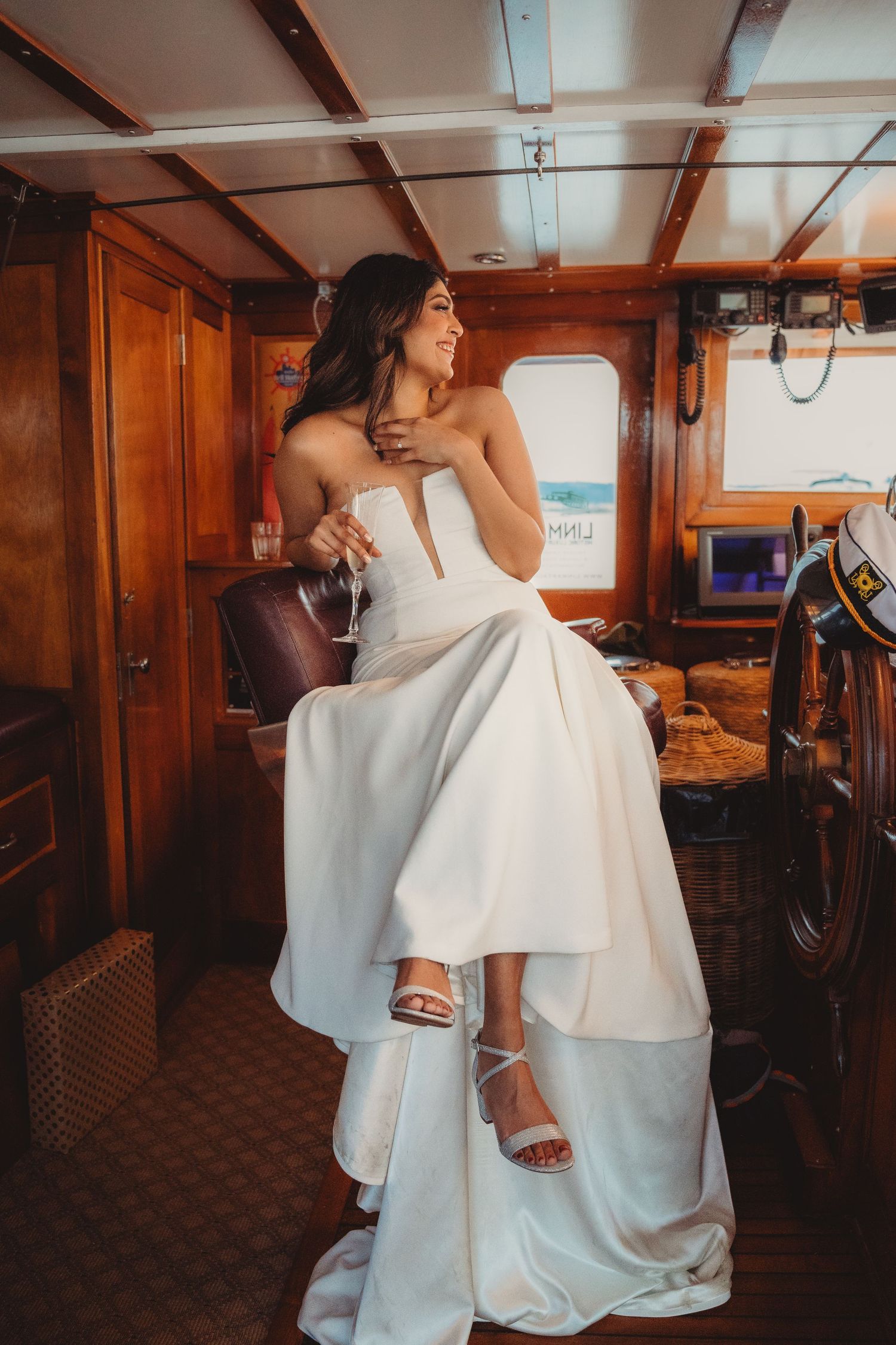 Elegant bride in a strapless white gown sitting inside a luxury wooden yacht holding champagne. Charleston South Carolina