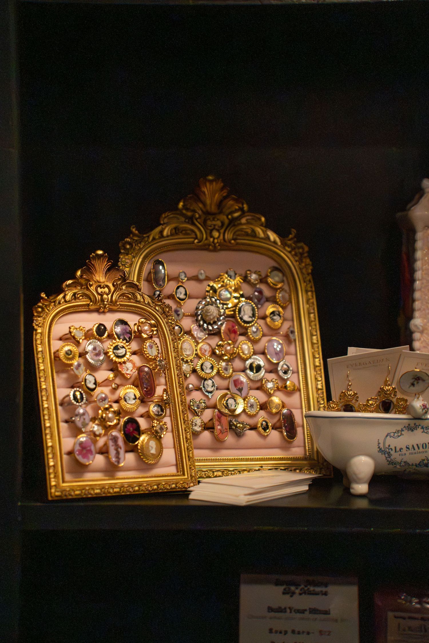 Ornate gold frames displaying colorful gemstone rings on a dark shelf.
