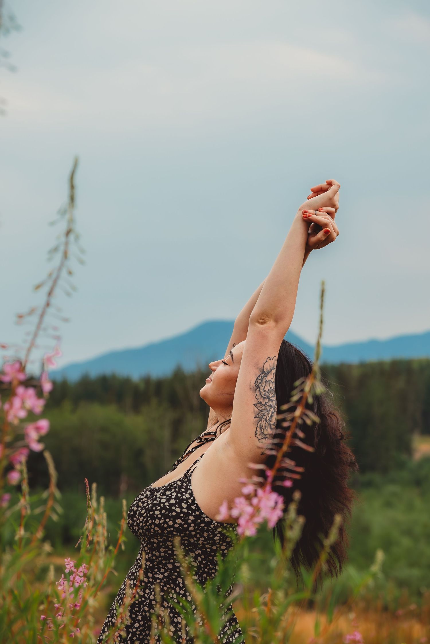 Woman with tattoo in floral dress reaching arms up in wildflower meadow.  mount Rainer