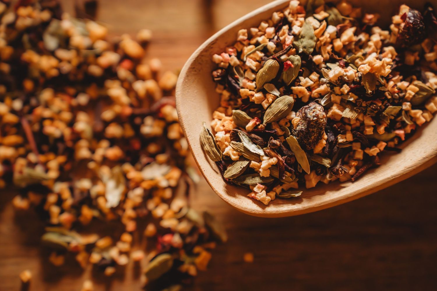Close-up of aromatic loose herbal tea blend with seeds and dried botanicals in a wooden spoon.