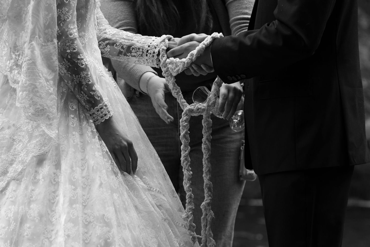 Black and white photo of bride and groom exchanging rings during a wedding handfasting ceremony.