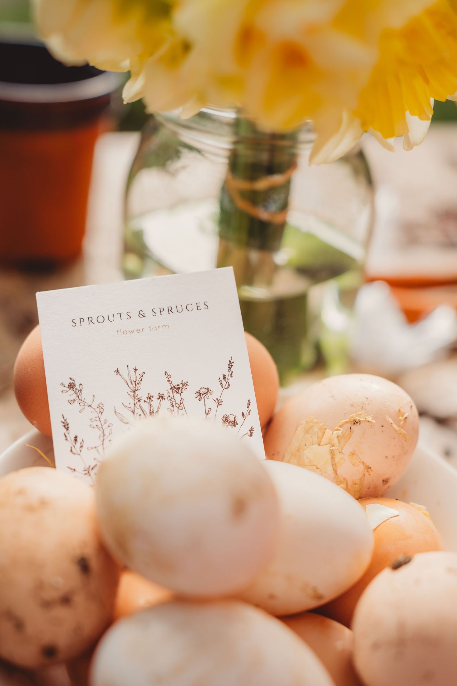 Sprouts & Spruces flower farm card resting on fresh eggs with yellow daffodils in a mason jar in background.