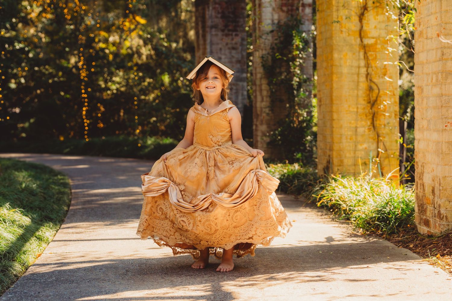 Little girl twirling in golden princess gown on sunlit garden pathway.Summerville South Carolina