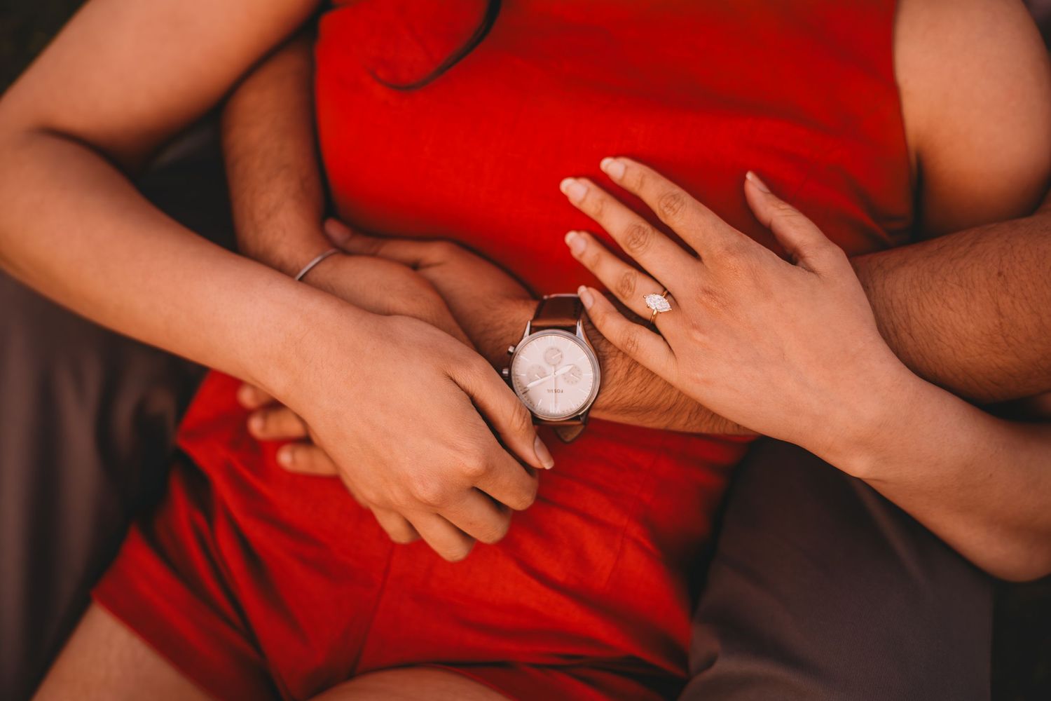 Close-up of a couple embracing, one wearing a leather watch, dressed in red and neutral tones.