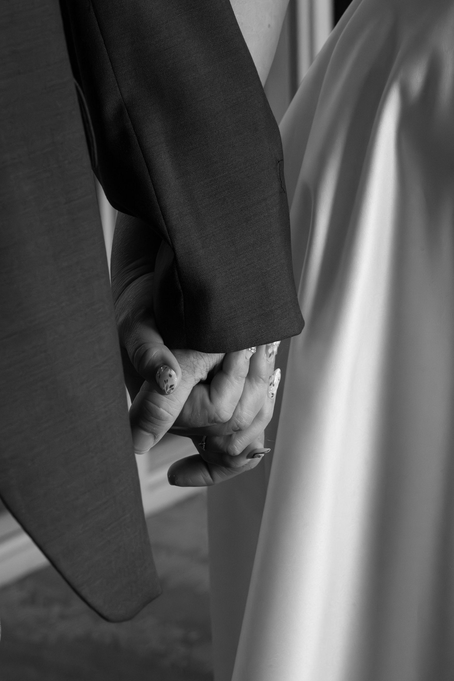 Black and white close-up of bride and groom holding hands in wedding attire. Arkansas