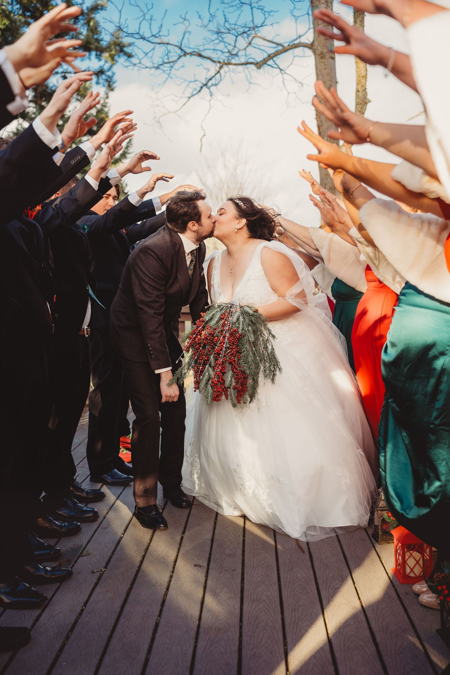 Bride and groom kiss while guests raise hands in celebration on a wooden deck at outdoor wedding ceremony. tacoma Washington