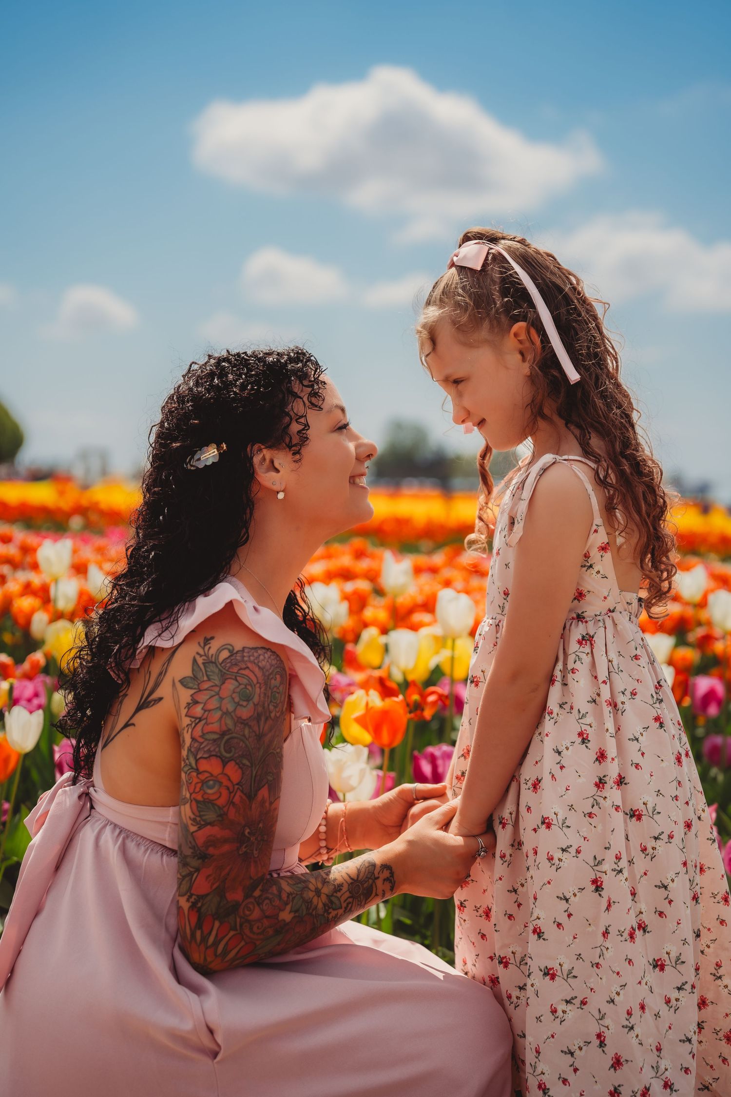 Mother with tattoos and daughter holding hands smiling in a colorful tulip field under blue sky. skagit valley