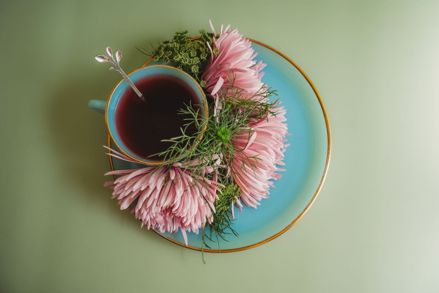 Top view of blue teacup with pink chrysanthemums on gold-rimmed saucer, green background.