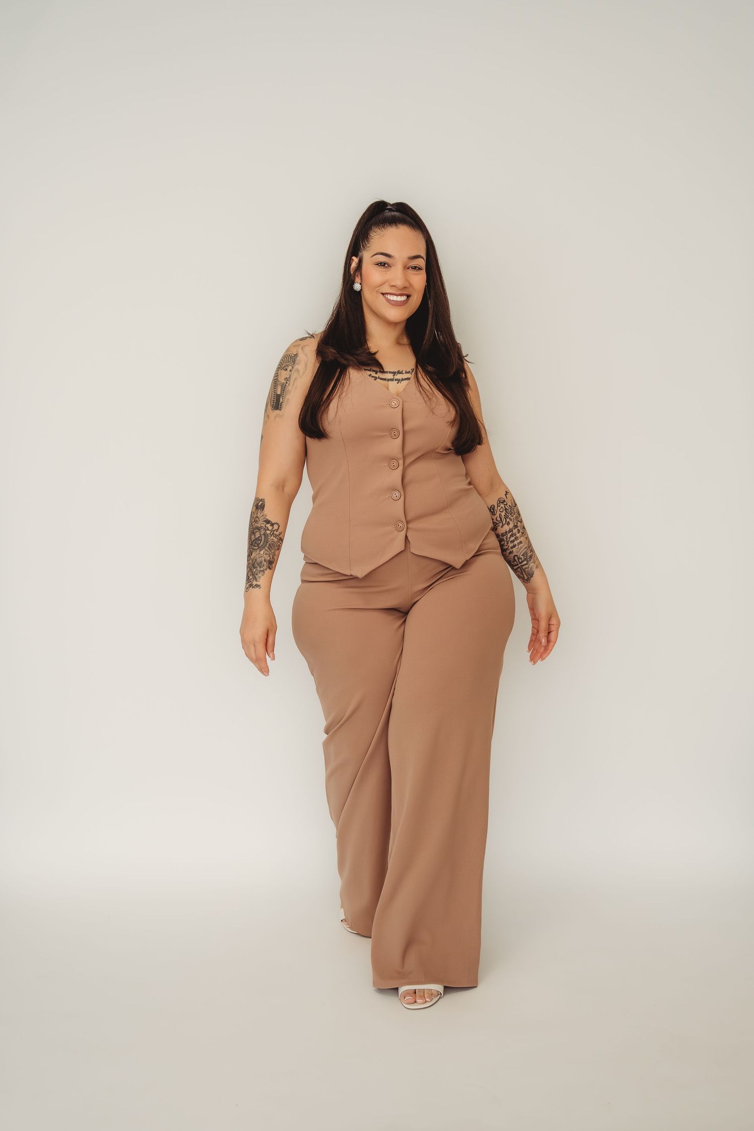 Smiling plus-size woman with tattoos wearing a beige sleeveless vest and wide-leg pants set. Branding photos South Carolina