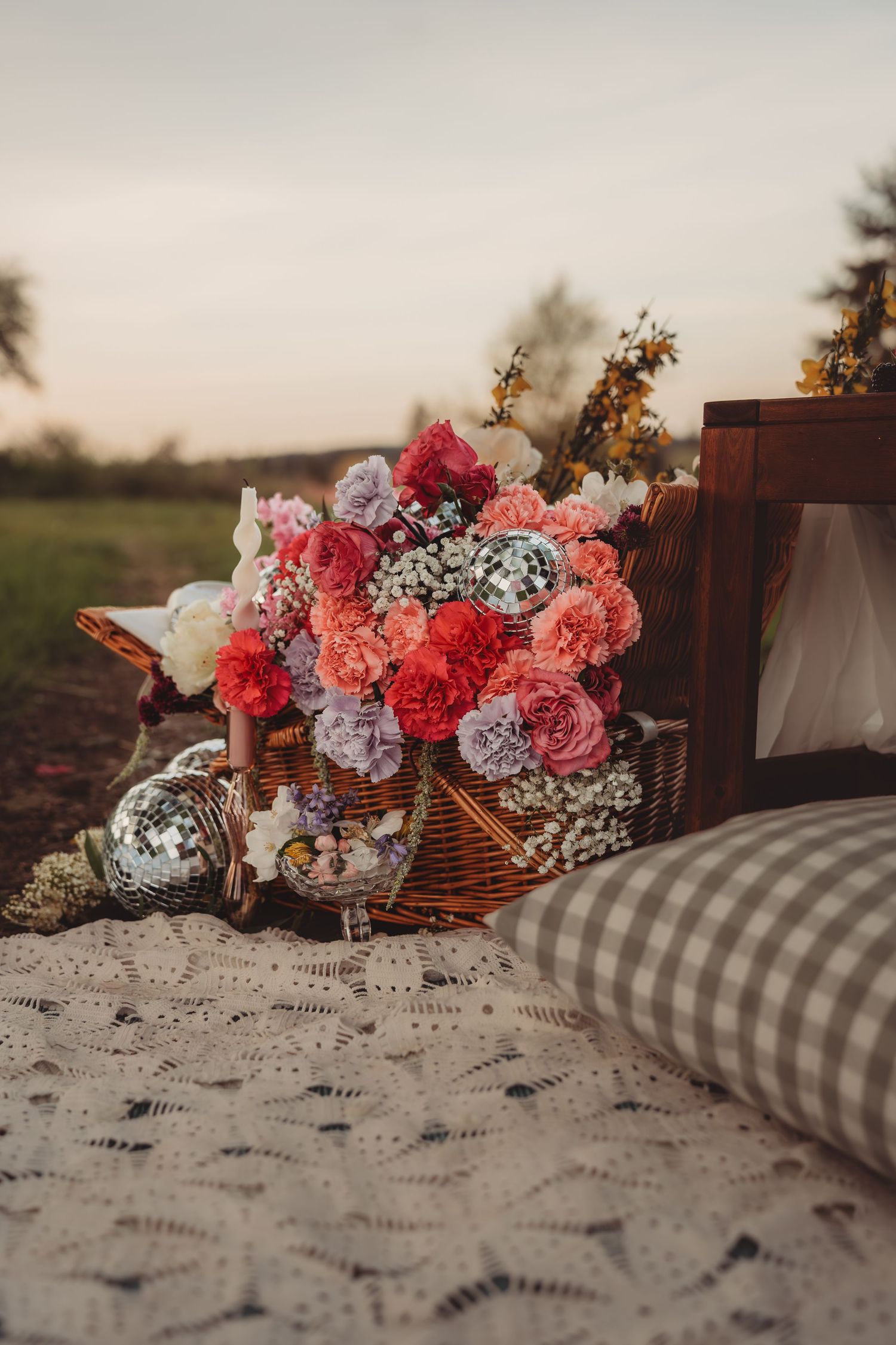 A wicker basket filled with colorful pink, red, and purple flowers on a lace blanket at a romantic outdoor picnic.