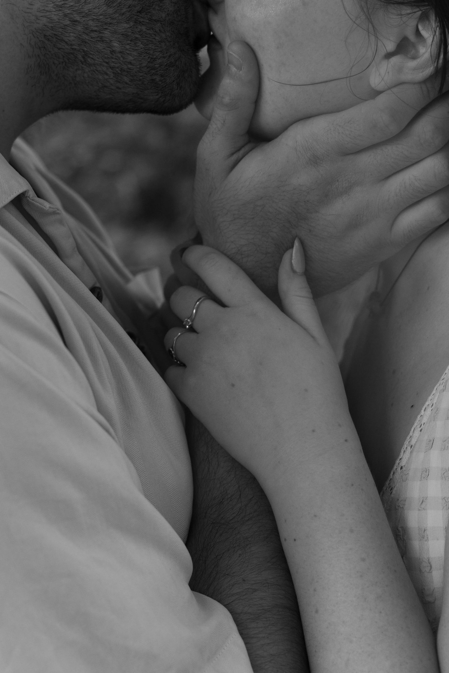Black and white photo of a couple sharing an intimate kiss, with a woman's ringed hand gently touching a man's face.