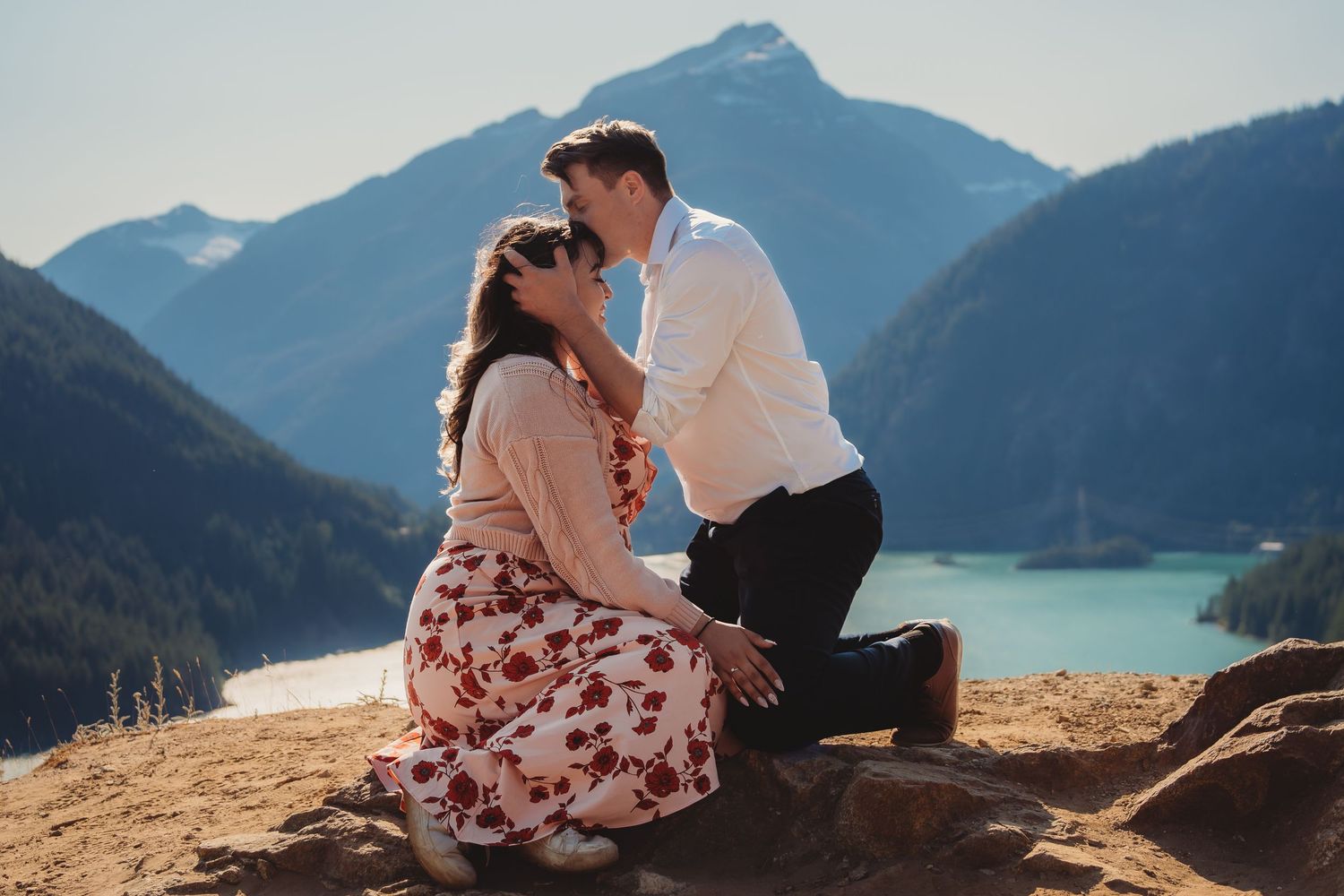 Man on one knee proposing to woman on rocky overlook with stunning mountain lake scenery in background. cascade mountain national park