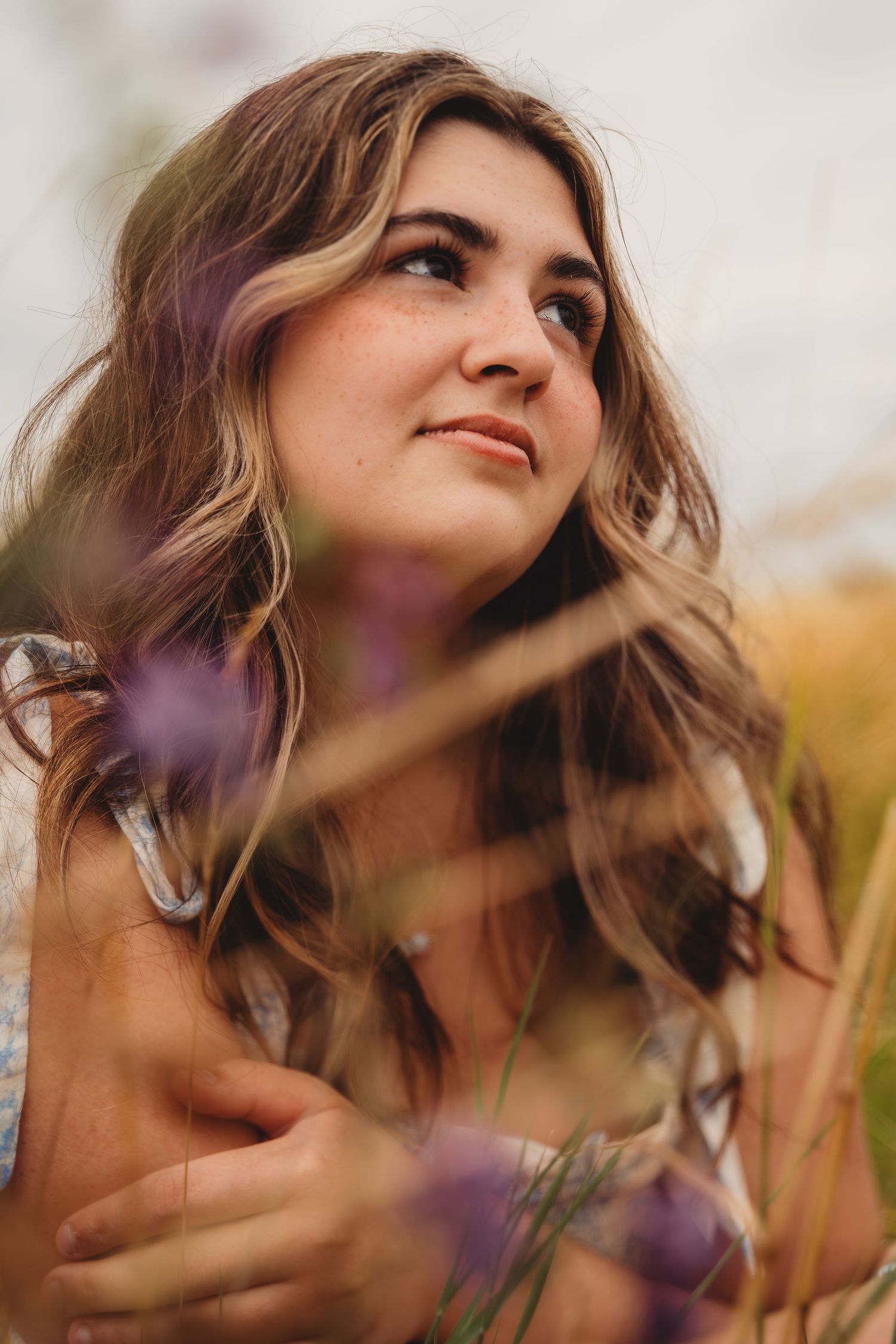 Young woman with wavy highlighted hair gazing upward surrounded by purple wildflowers in golden field.Charleston South Carolina