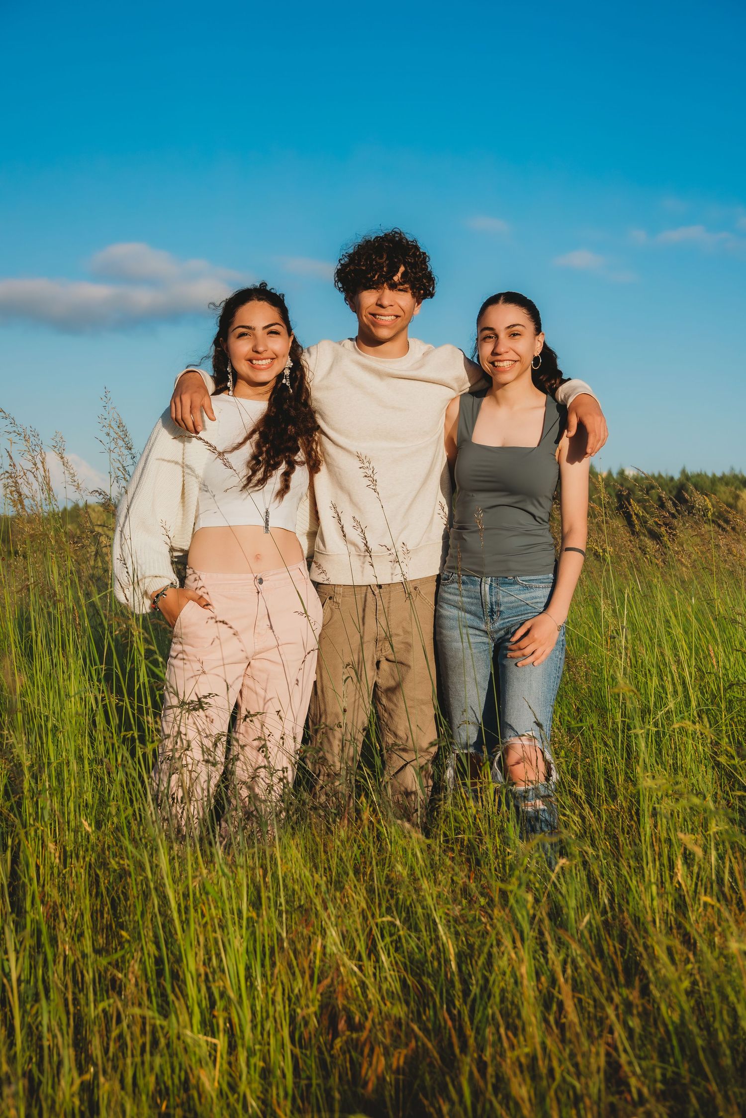 Three smiling friends posing together in a green field under a blue sky. Seattle