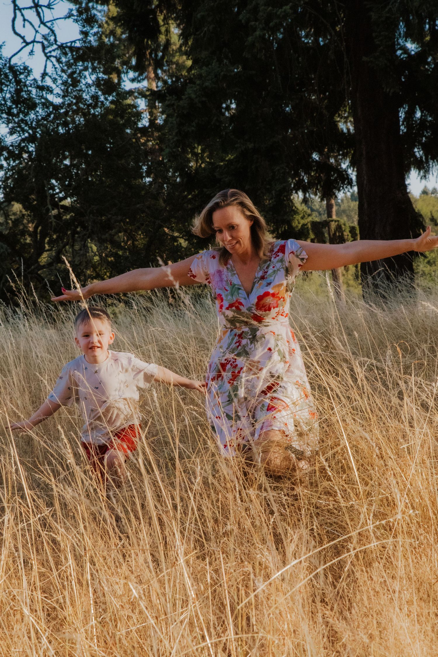 Joyful mother jumping in golden field while holding hands with her laughing toddler son. Washington