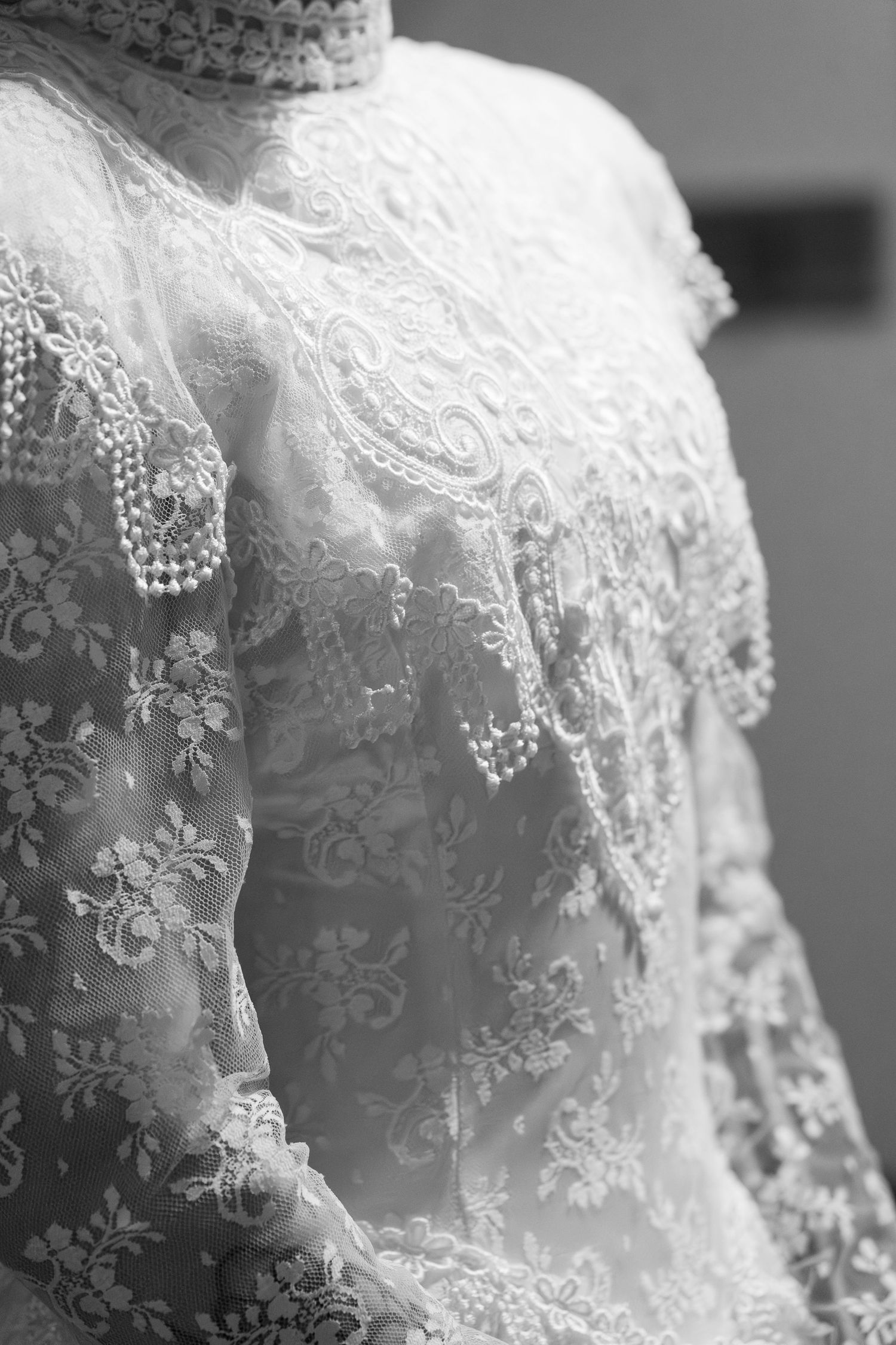 Close-up black and white photo of intricate lace wedding dress with pearl embellishments on a mannequin.