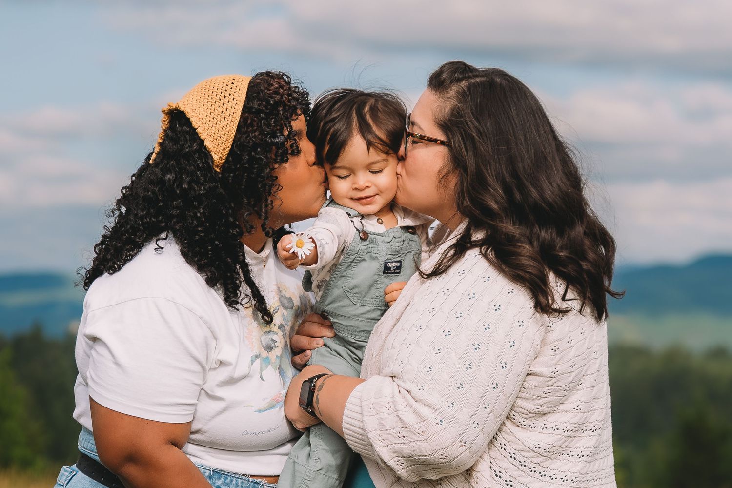 Two women kissing happy baby outdoors with scenic green hills in background.Summerville South Carolina